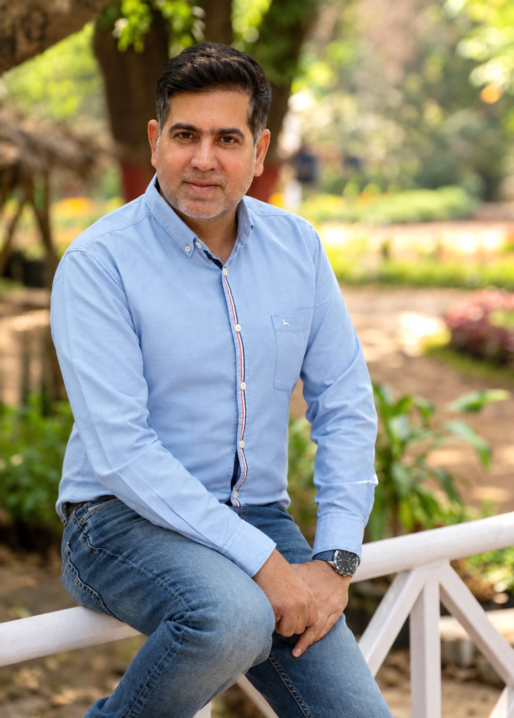 Portrait of Sachin Malhotra sitting on a white railing in a garden
